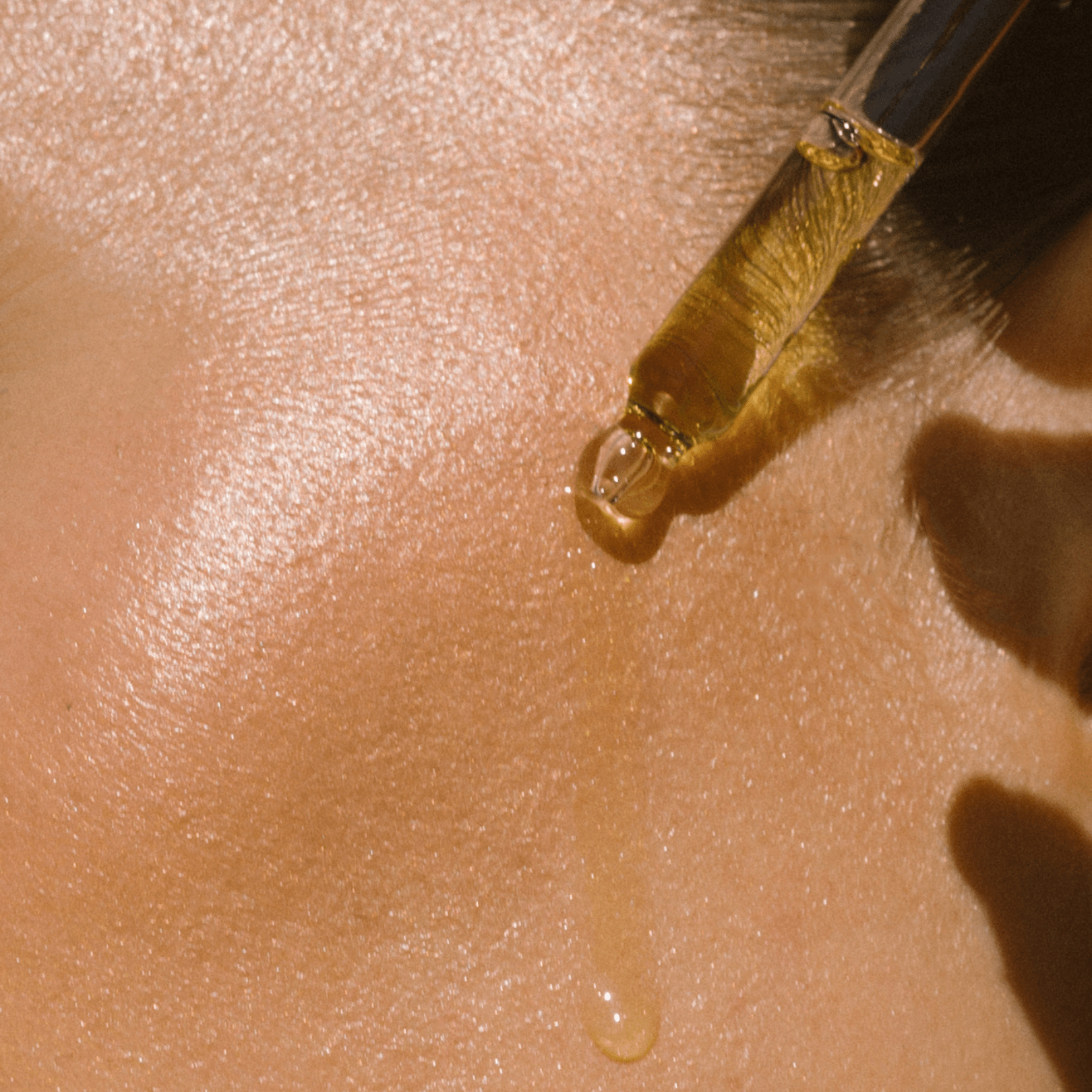 Close-up of dropper releasing a drop of Eco By Sonya Glory Oil onto smooth hydrated skin, showing rich golden oily texture.